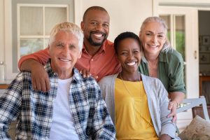 Senior couple with mature man and african woman posing for a photo sitting at courtyard. Portrait of happy multi ethnic people sitting on couch under patio. Cheerful men and beautiful women looking at camera.